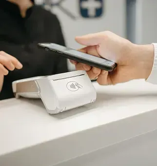 A person uses a smartphone for contactless payment over a white payment terminal.