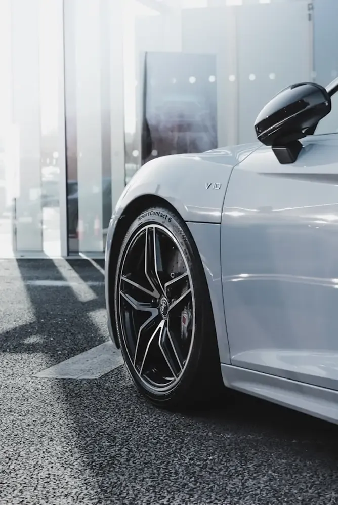 Close-up of a white luxury sports car's front wheel and fender, sleek design.