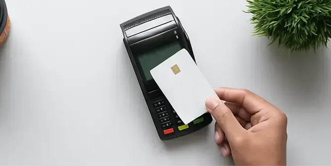 Hand holding a white contactless payment card near a black POS terminal.