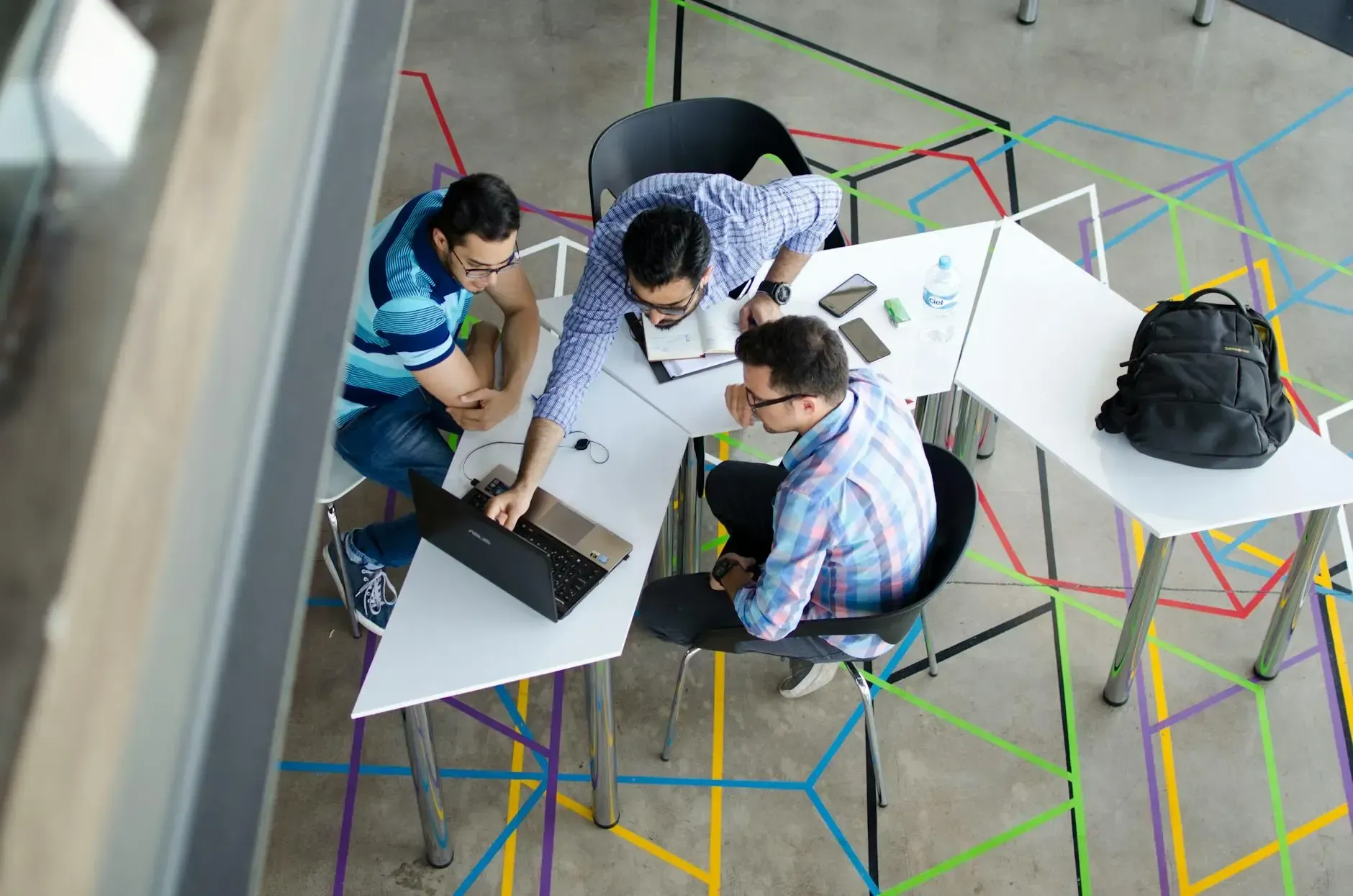 Four men collaborate around a modern desk with a laptop in an office.