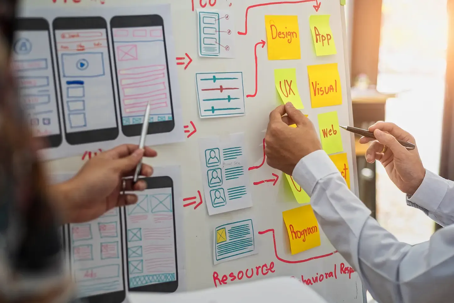 Two designers collaborate on a whiteboard, planning mobile application user interfaces and user experience.
