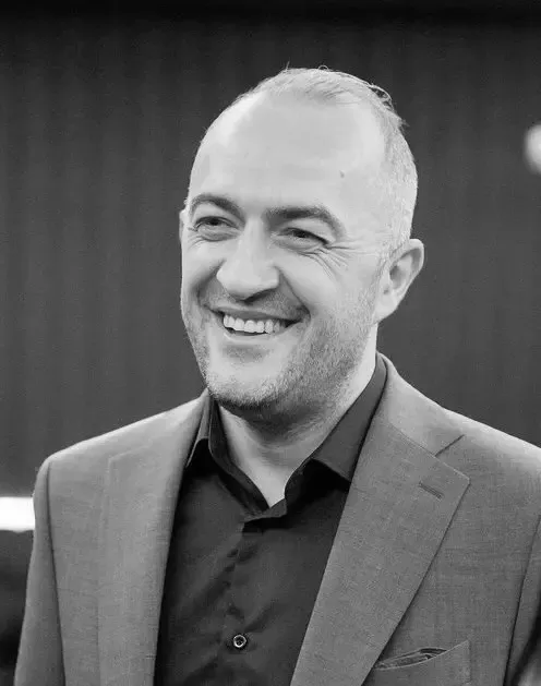 Bald man in a dark suit jacket smiling, looking toward the right.