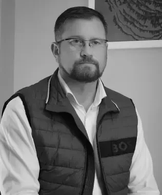 Black and white headshot of a man with a beard, glasses, and a vest.