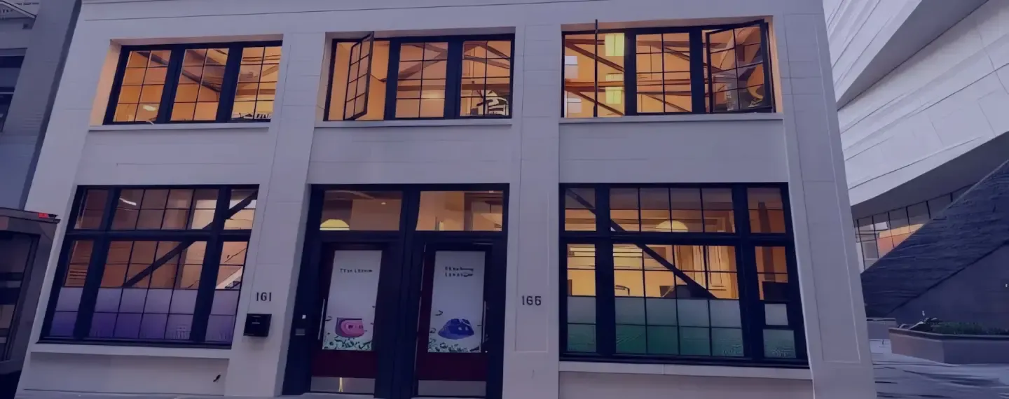 Modern two-story building with large illuminated windows at dusk in an urban setting.