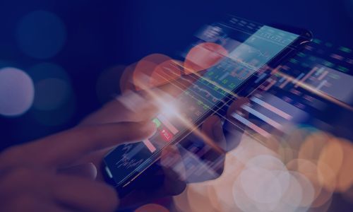 A hand interacts with a glowing smartphone displaying financial data charts, surrounded by blurred lights.
