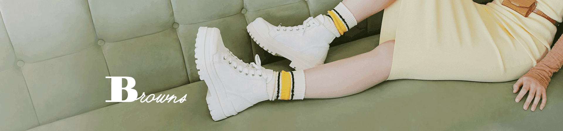 Person on a green sofa wearing white high-top sneakers, yellow-striped socks, and 'B Towns' apparel.