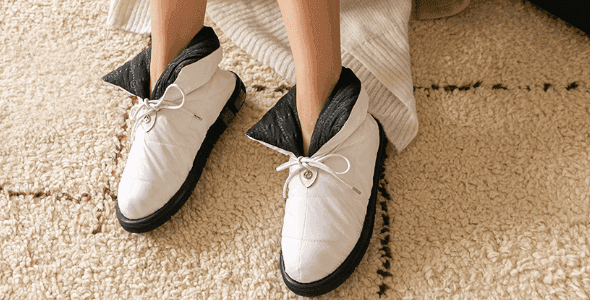 White puffy boot-style slippers with black soles worn on a cream textured rug.