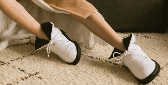 Person wearing white and black casual shoes with black soles, sitting on a textured rug.