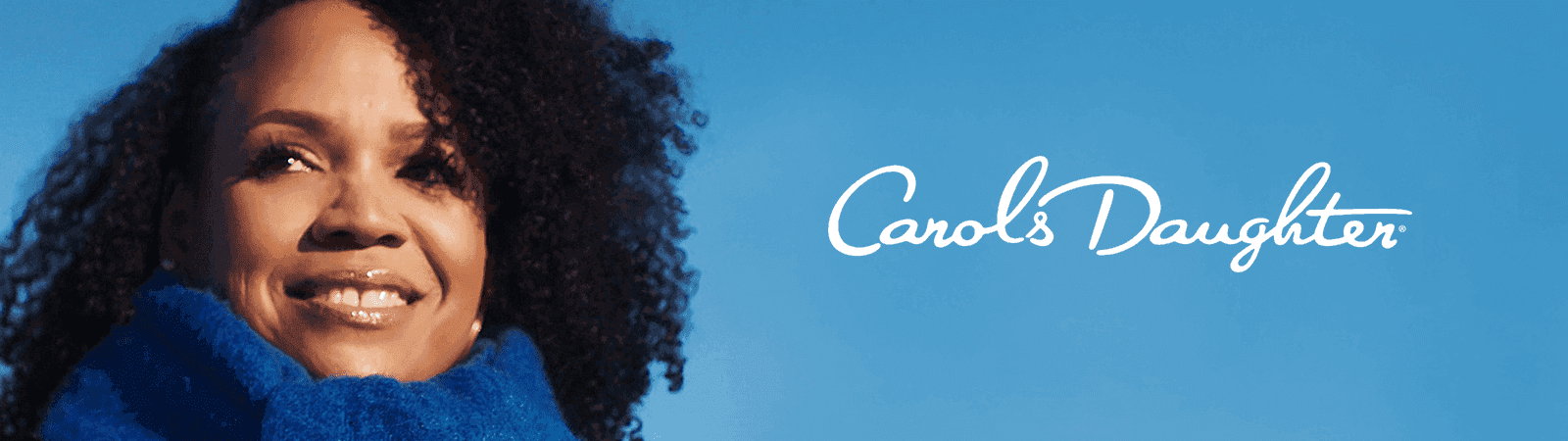 Smiling woman with curly hair and blue scarf against a blue sky, "Carol's Daughter" logo.