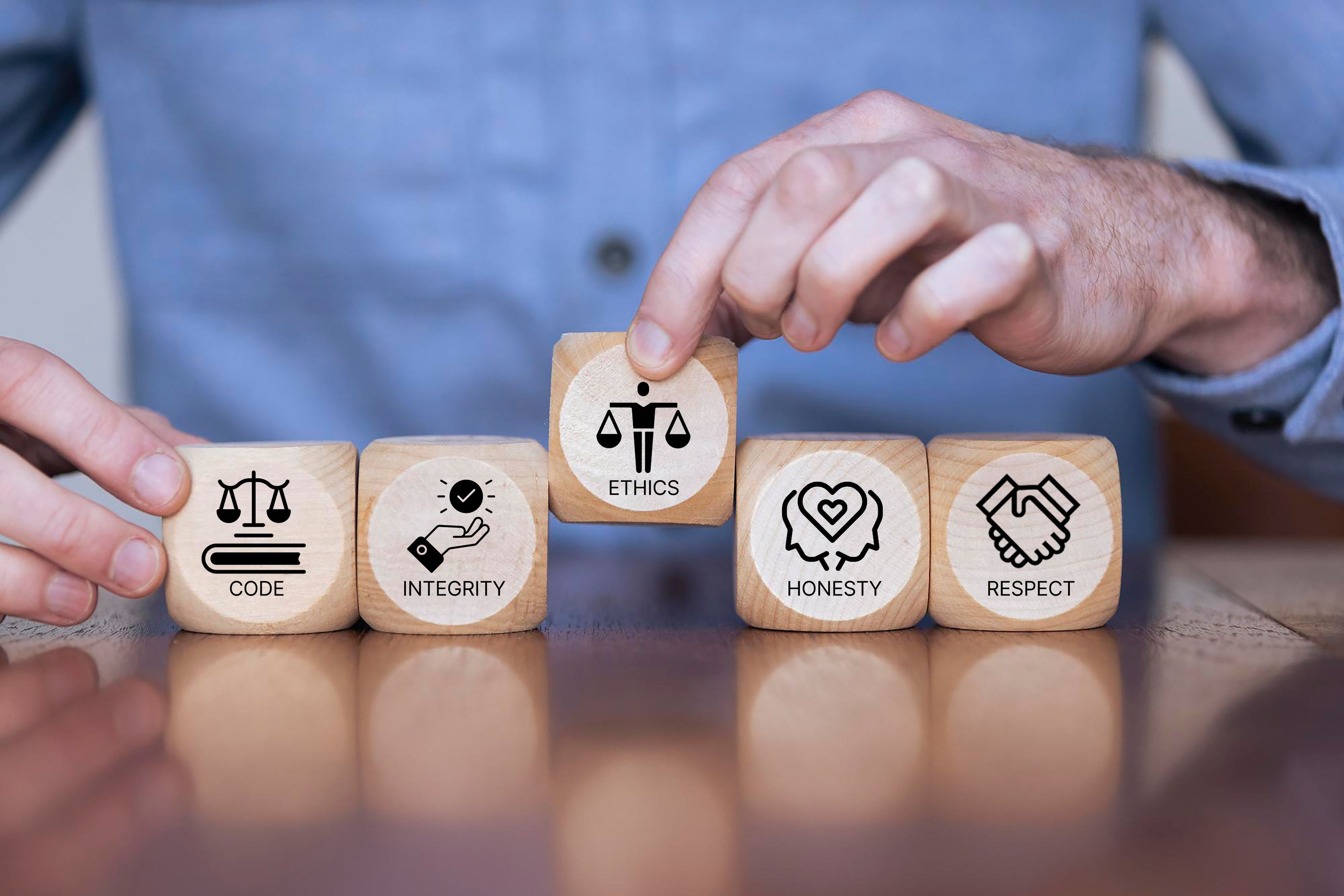 Hands arranging wooden blocks depicting ethics, integrity, honesty, code, and respect concepts.