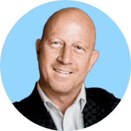 Headshot of a smiling bald man with blue eyes, wearing a white shirt and dark jacket.