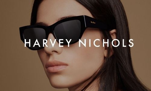 Woman wearing large black sunglasses with HARVEY NICHOLS branding on the lenses.