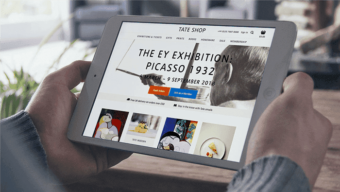 A person holds a tablet displaying the Tate Shop website promoting a Picasso exhibition.