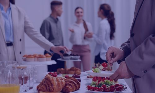 Guests serving themselves from a buffet table with pastries, fruit, and small bites.