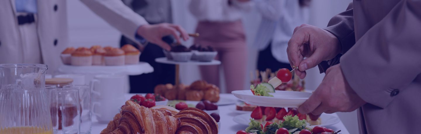 Guests serving themselves from a buffet table with pastries, fruit, and small bites.