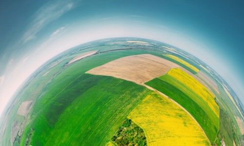Aerial fisheye view of vibrant green, yellow, and brown agricultural fields under a clear blue sky.