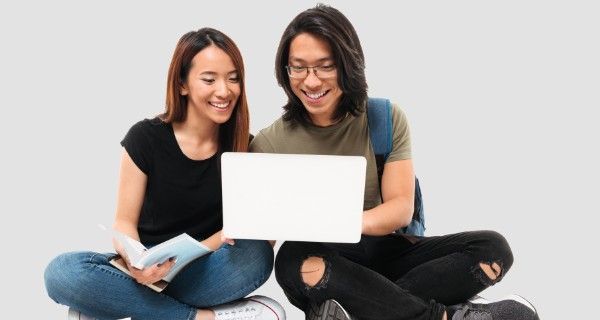 Two smiling students collaborate on a laptop, one holding a notebook.