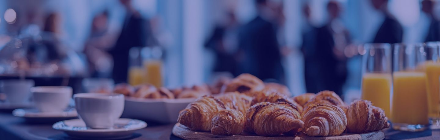 Croissants, coffee cup, and orange juice on a table with blurred people in the background.