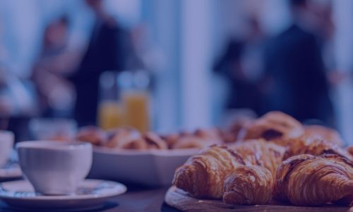 Croissants, coffee cup, and orange juice on a table with blurred people in the background.