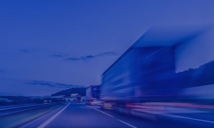Blurred trucks on a highway at dusk, showing motion and light trails.
