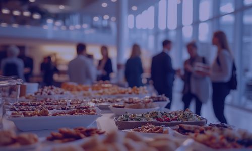 A buffet table filled with various appetizers and desserts, with guests mingling in background.