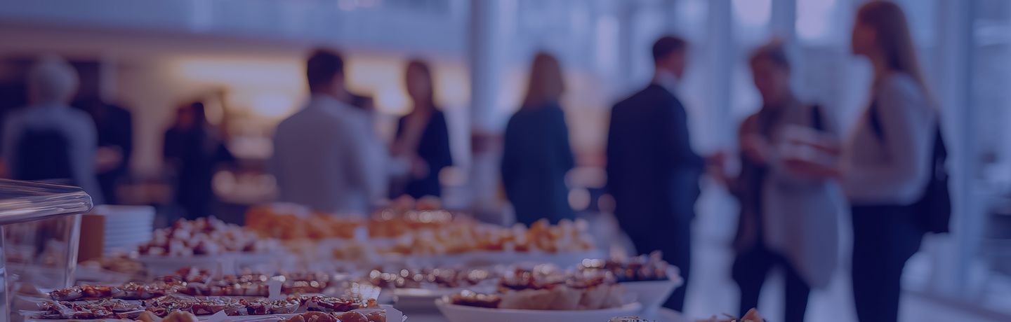 A buffet table filled with various appetizers and desserts, with guests mingling in background.